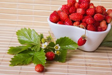 Wall Mural - Wild strawberries in a small bowl, surrounded by leaves