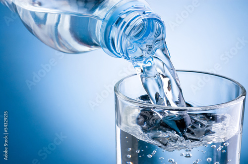wlewanie-wody-z-butelki-do-szklanki-na-niebieskim-tle