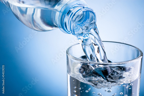 Obraz w ramie Pouring water from bottle into glass on blue background