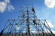 Workers working on tall scaffolding against a blue sky