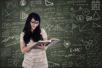 Wall Mural - Asian female student reading book on chalkboard background