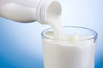 Wall Mural - Pouring milk from white plastic bottle into glass on blue backgr