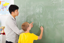 Elementary School Teacher Helping Young Boy Writing Chinese