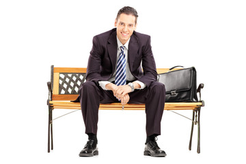 Wall Mural - Smiling young businessman sitting on a wooden bench