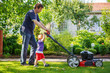 Man and his little son having fun with lawn mower in garden