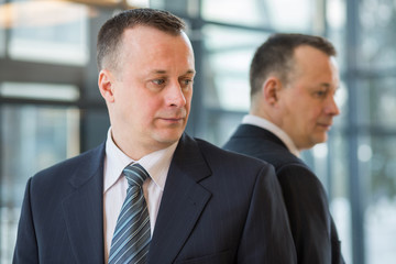 businessman in suit and tie stands near a mirror