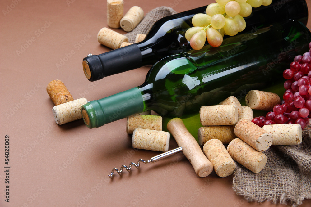 Bottles of wine, grapes and corks on brown background