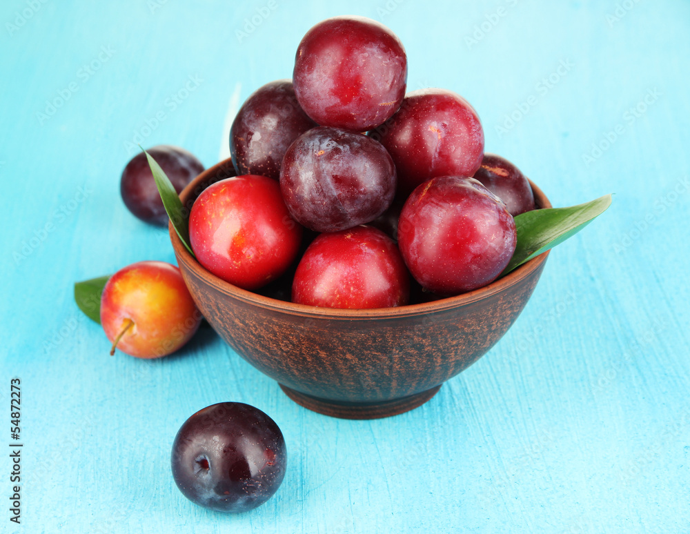 Ripe plums in bowl on wooden table close-up