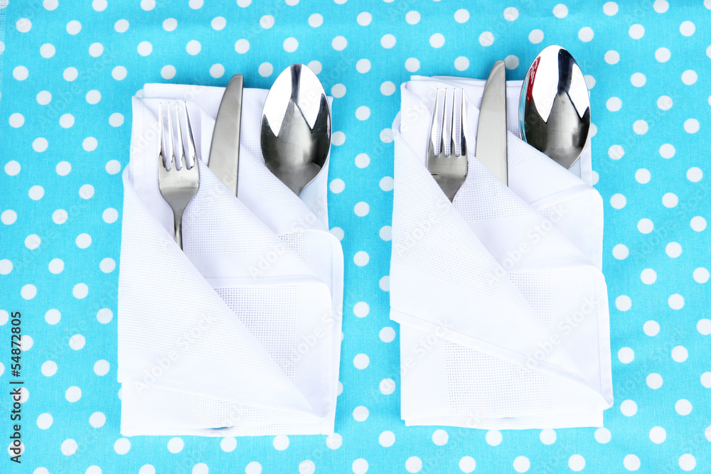 Folded napkin with fork, spoon and knife on color background
