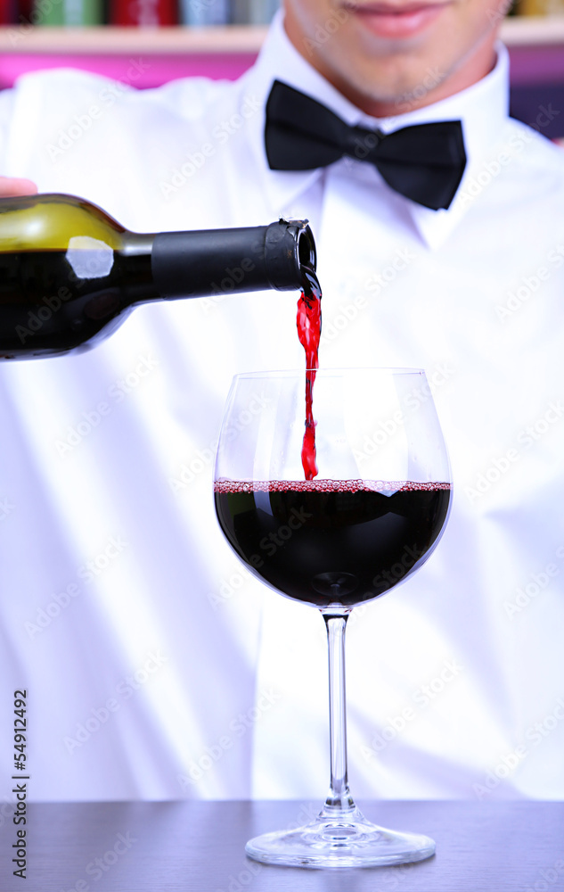 Bartender is pouring red wine into glass