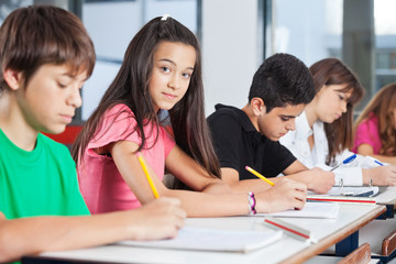 teenage girl sitting with classmates writing at desk