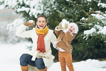Wall Mural - Happy mother and baby throwing snowballs in winter park