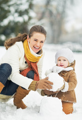 Wall Mural - Happy mother and baby making snowman in winter park