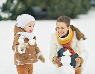 Wall Mural - Happy mother and baby making snowman in winter park