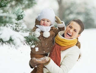 Wall Mural - Happy mother and baby playing with snow on branch