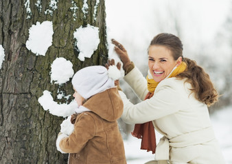 Wall Mural - Happy mother and baby making face for tree using snow