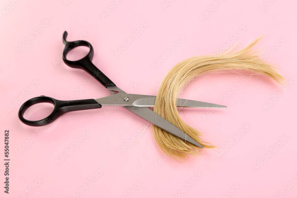Pieces of hair cut with scissors on pink background