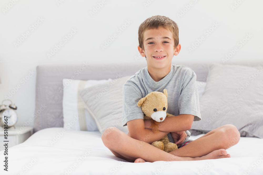 Smiling little boy sitting on bed holding his teddy bear Stock Photo ...