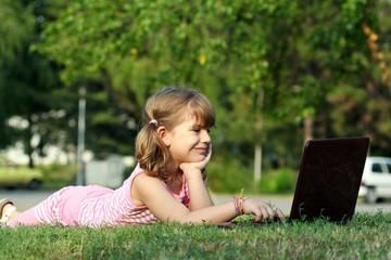 Wall Mural - little girl lying on grass with laptop