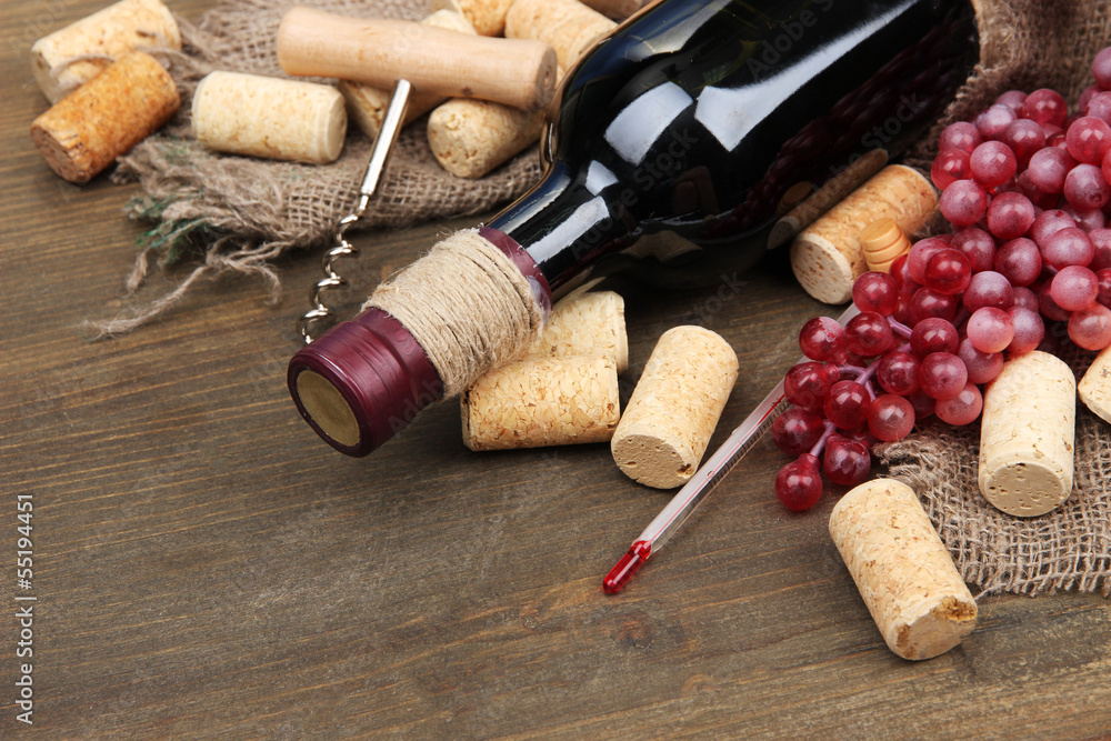Bottle of wine, grapes and corks on wooden background