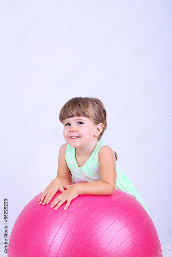 Little cute girl playing with big ball, on gray background