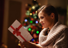 Happy Young Woman Reading Postcard In Front Of Christmas Tree