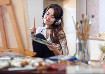 Long-haired woman in headphones  paints on canvas