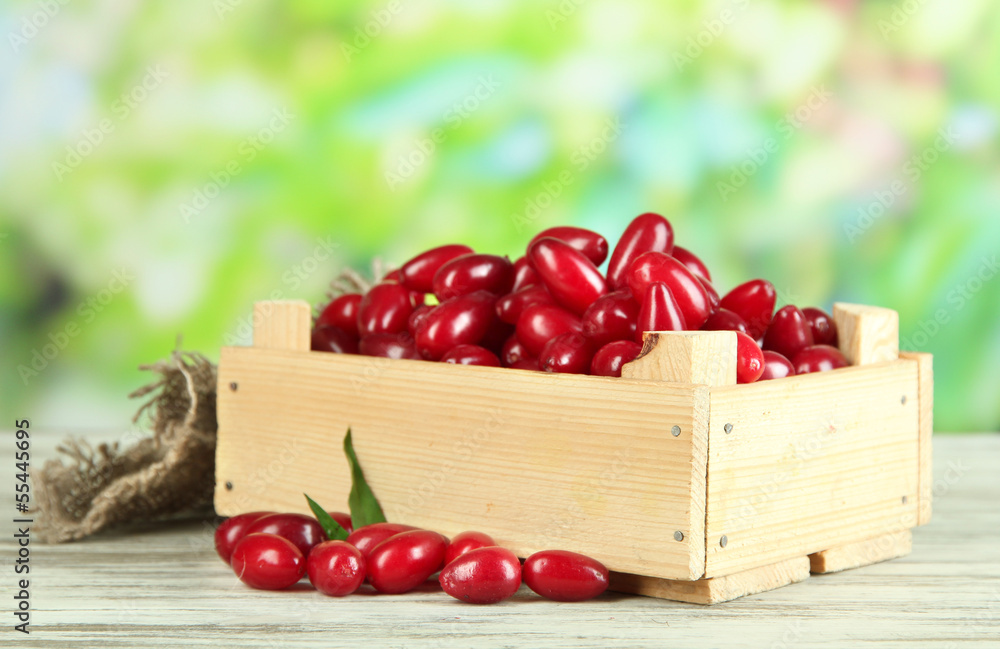 Fresh cornel berries in wooden crate on table, outdoors