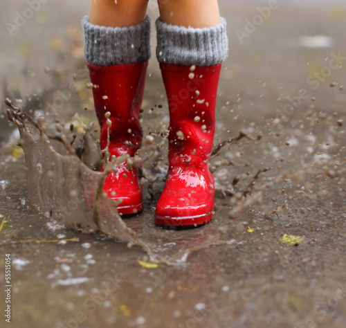 Fotografie, Obraz Child wearing red rain boots jumping into a puddle