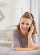© Alliance - Happy young woman talking mobile phone in living room