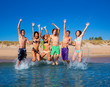 © lunamarina - Happy excited teen boys and girls beach jumping