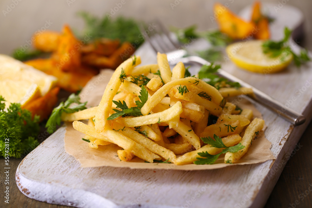 French fries on tracing paper on board on wooden table