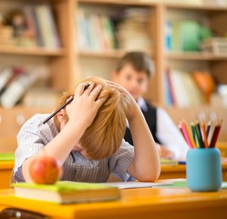 Fototapete - Little redhead schoolboy behind school desk