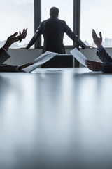 Two business people discussing and gesturing over the table while another looks out the window, hands only