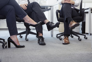 Three business people with legs crossed sitting on chairs, low section