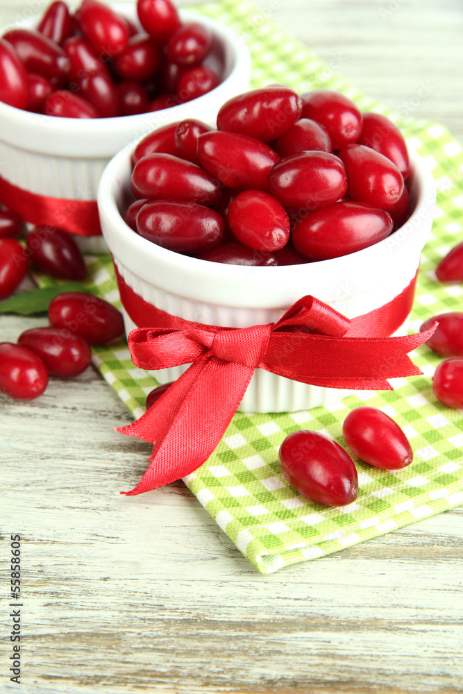 Fresh cornel berries in white cups on wooden table