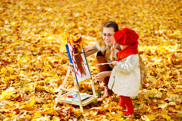 Mother and child drawing on easel in autumn park. Creative kids