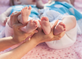 Legs newborns in parents hand. Twins lying on a pink blanket.