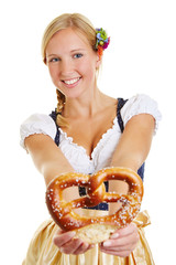 Happy woman in dirndl offering pretzel