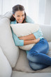 © lightwavemedia - Cheerful woman holding pillow sitting on couch