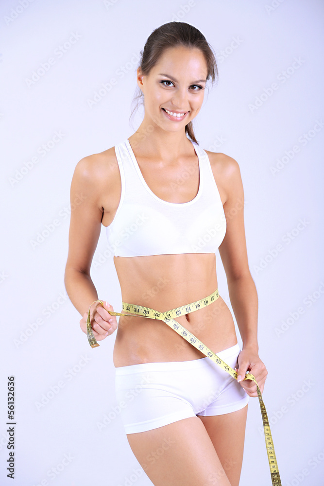 Slim girl with centimeter on gray background
