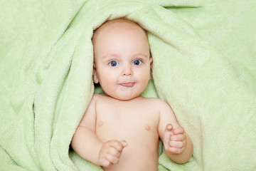 Caucasian baby boy covered with green towel joyfully smiles at c