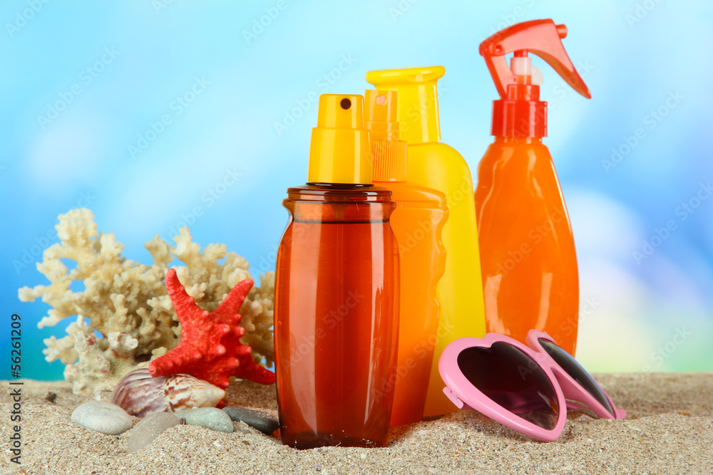 Bottles with suntan cream and sunglasses, on blue background