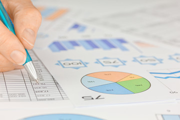 Hand with Pen working on Spreadsheet and Graphs