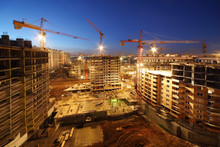 Lots Of Tower Cranes Build Large Residential Buildings At Night.