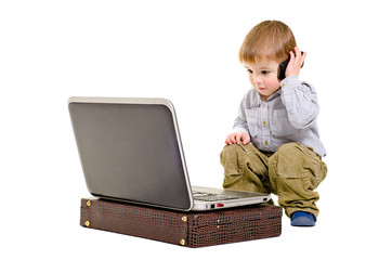 Cute boy speaks on a mobile phone looking at laptop