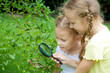 © altanaka - Two little girls with magnifying glass outdoors in the day time