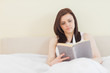 © WavebreakmediaMicro - Concentrated girl reading a book lying on a bed