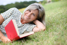 Senior Woman Reading Book Laid On The Grass