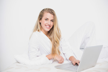 Wall Mural - Cheerful pretty model using her laptop lying on cosy bed